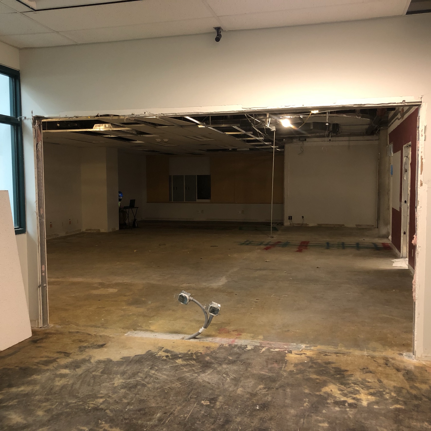 A photograph of a wall in the library that has been knocked out to reveal another room behind it which used to be the Exam Centre. This space will become the new Writing Centre and Makerspace. Flooring and ceiling covering have been removed exposing concrete and wiring.