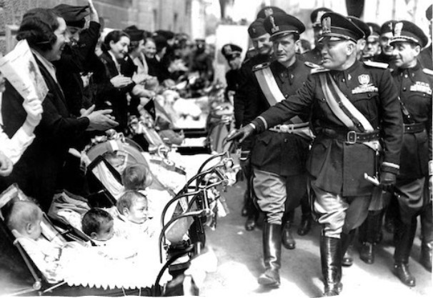 A group of military officers pass mothers with baby carriages during a parade